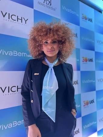Recepcionista uniformizada em frente ao painel da Vichy e VivaBem